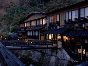 Un ryokan japonés tradicional con varias construcciones conectadas, un puente de madera y montañas al fondo.