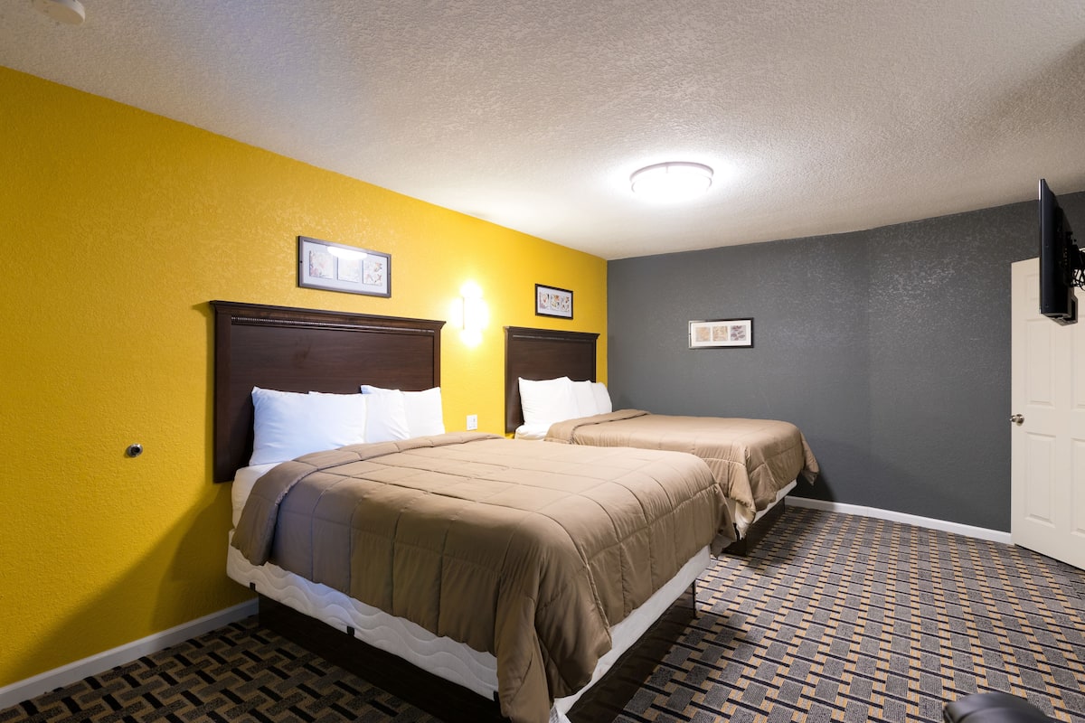 A hotel room with two beds, a patterned carpet, and a door.