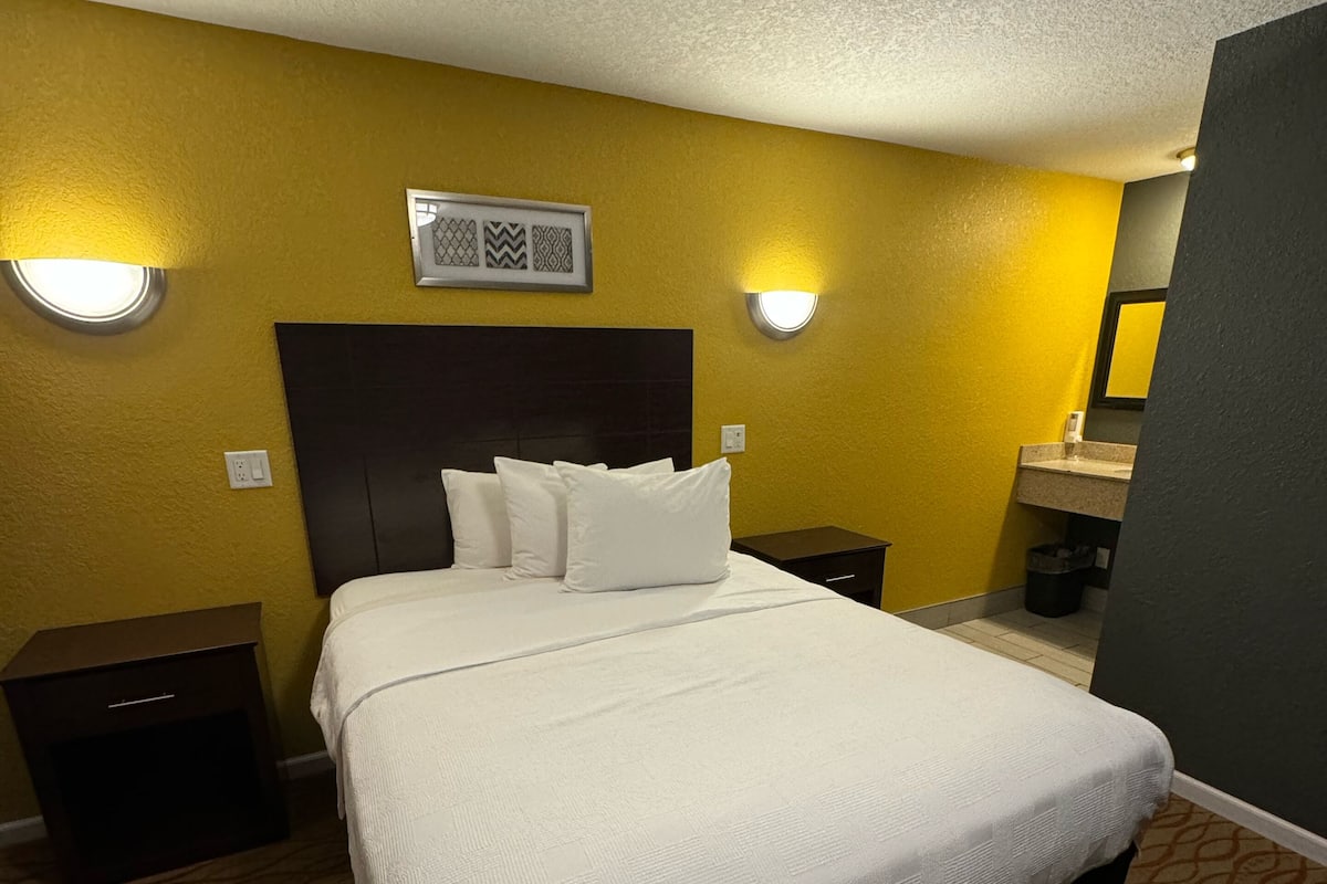 A hotel room with a large bed, two bedside tables, a headboard, and a wall-mounted light fixture.