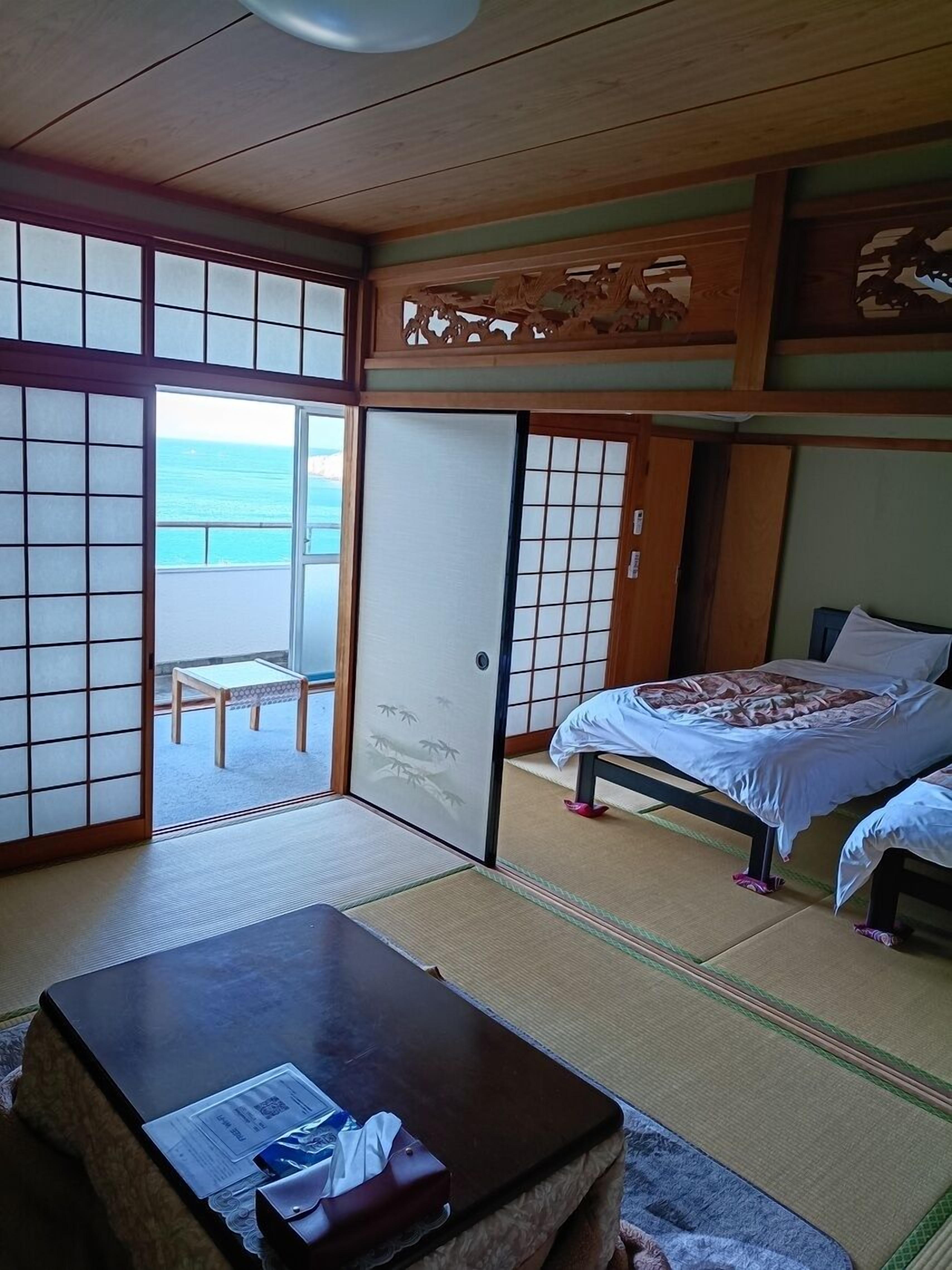 A traditional Japanese room with tatami flooring, a sliding door leading to a balcony, and a bed with a patterned bedspread.