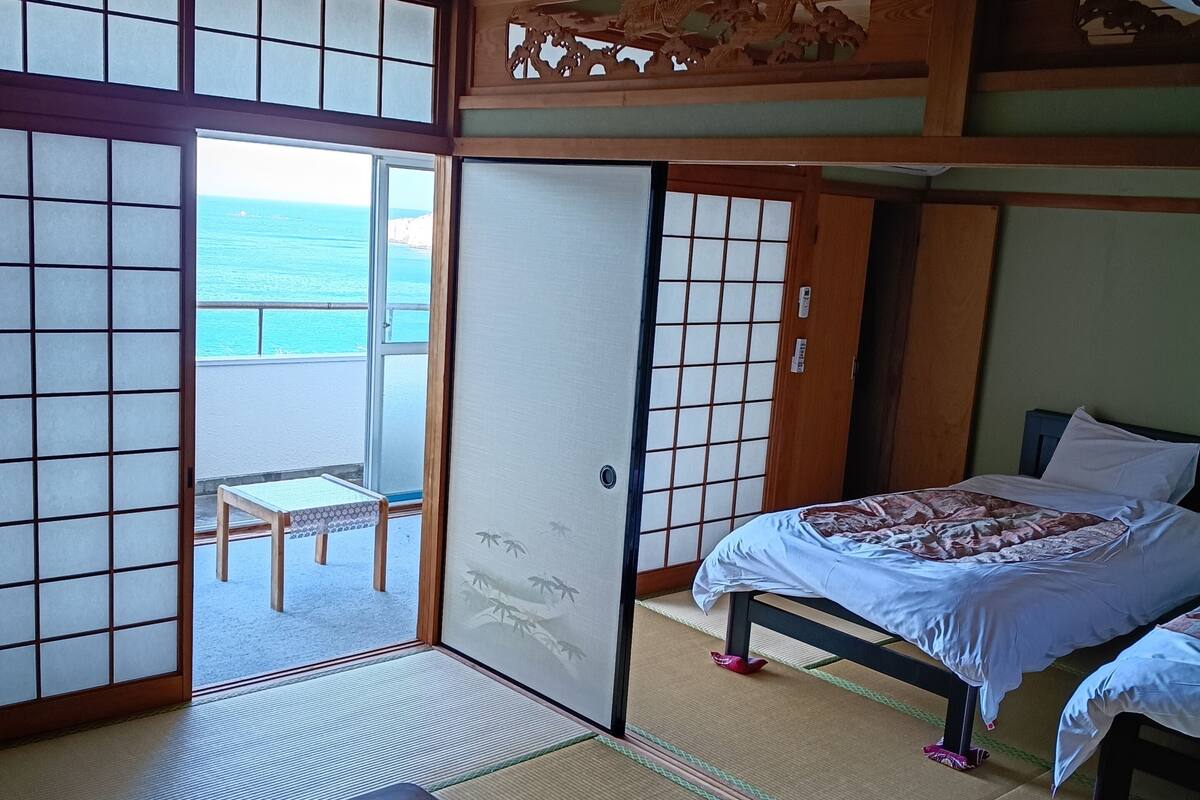 Een traditionele Japanse kamer met tatami vloeren, een schuifdeur naar een balkon en een bed met een geborduurde spreidekker.