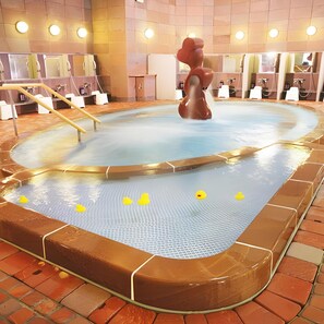 A hot tub with a unique sculpture in the center, surrounded by a tiled floor and a brick border. - Takanokono Hotel (Matsuyama)