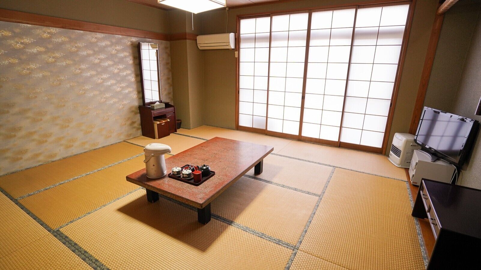 Una habitación con tatamis, una mesa baja, un set de té japonés tradicional, un espejo y puertas correderas.