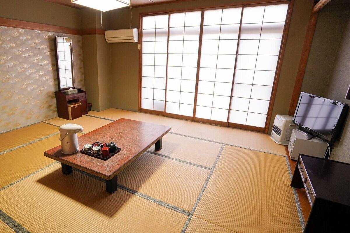 Una habitación con tatamis, una mesa baja, un set de té japonés tradicional, un espejo y puertas correderas.