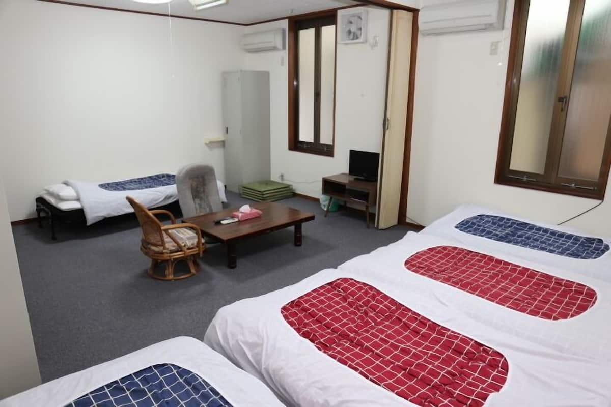 A hotel room with two beds, a chair, a small table, a TV, and a mirror.