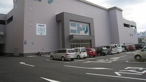 A building with a sign that reads 'ニトリ' and a parking lot with several cars.