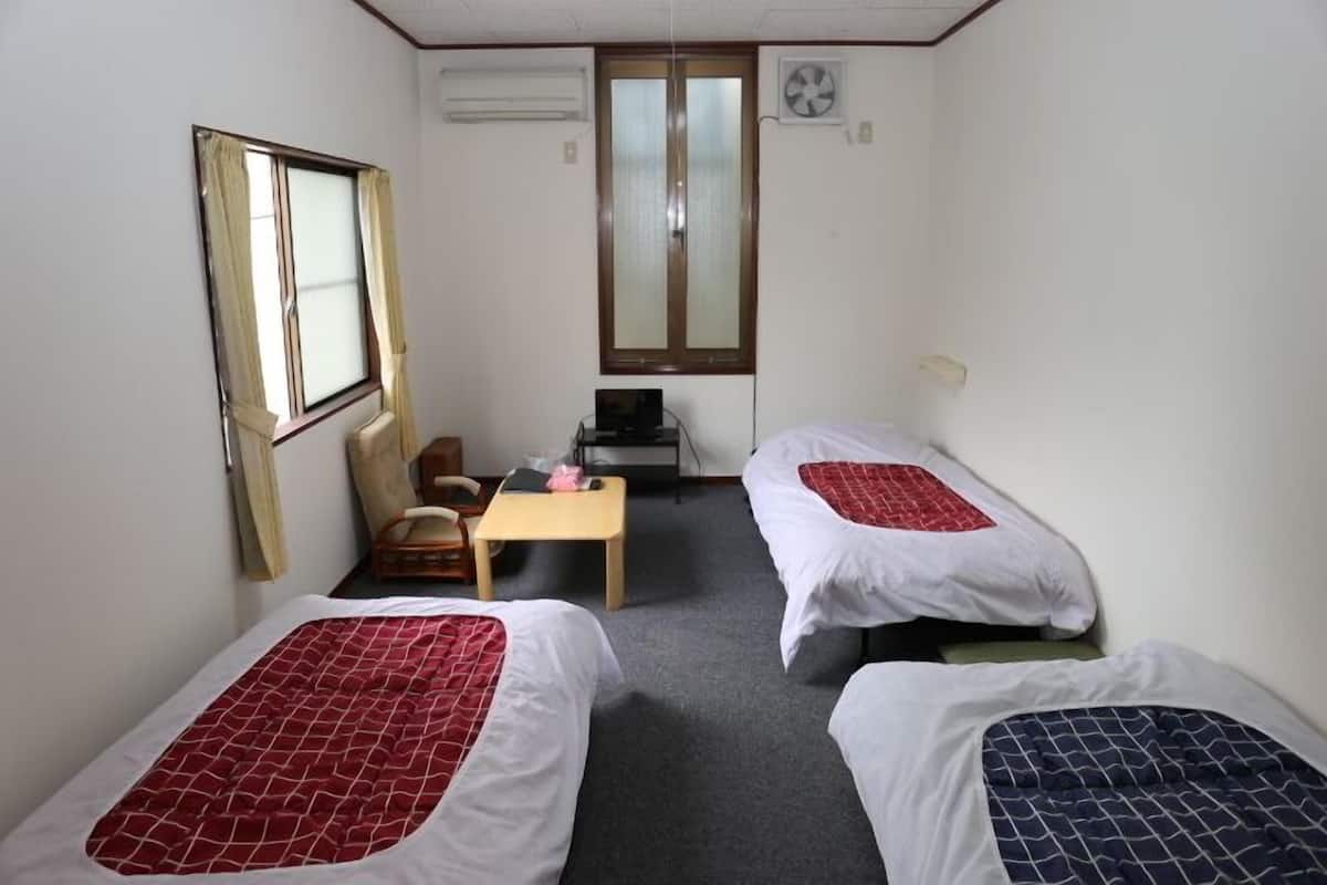 A small room with two single beds, a desk, a chair, and a window.