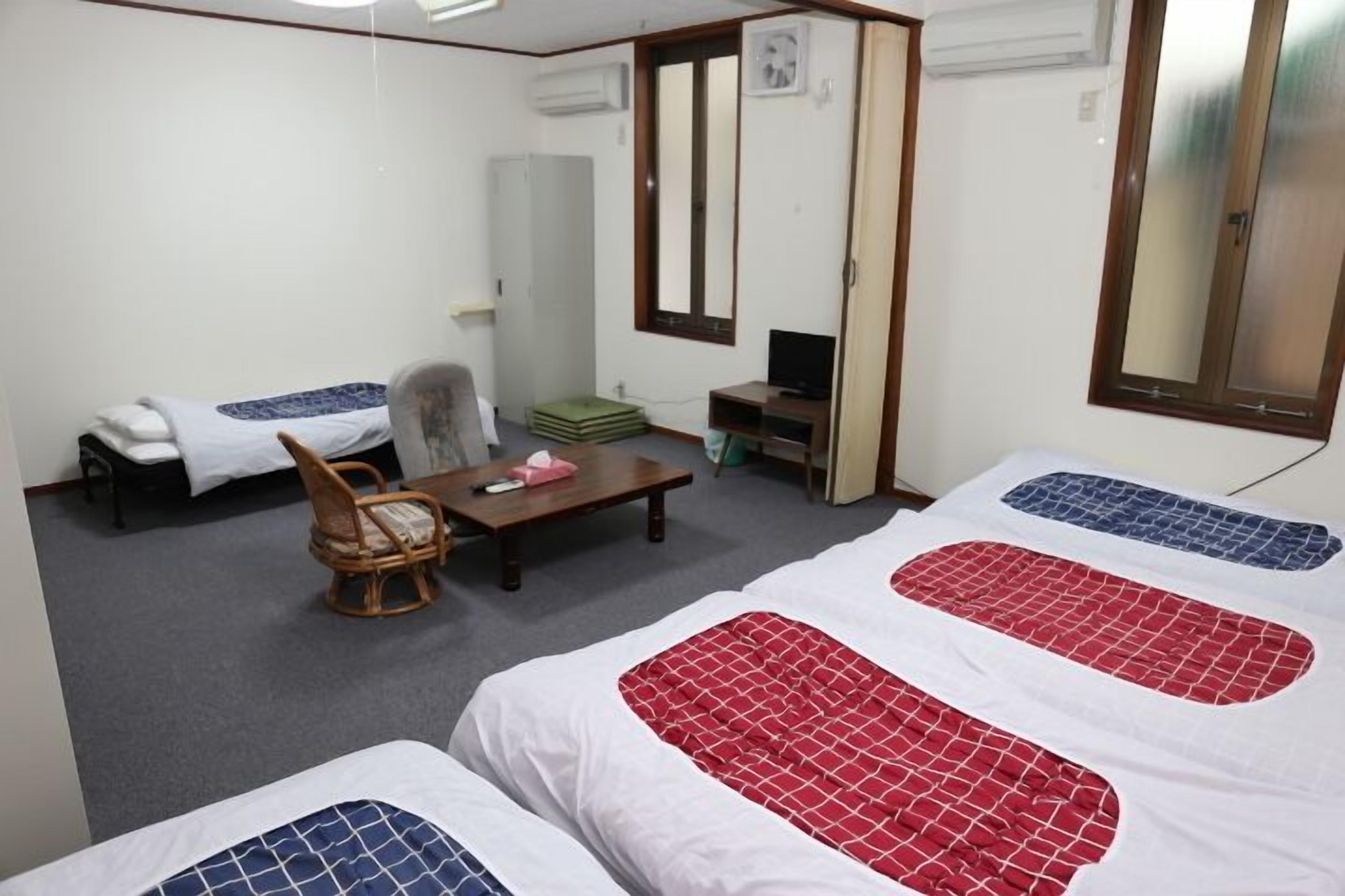 Een kamer met twee bedden, een stoel, een tafel, een televisie en een spiegel.