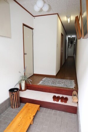 A narrow hallway with a wooden bench, a small rug, and a trash can.