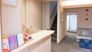 A reception area with a wooden counter, a staircase, a sofa, and a wall with emergency buttons.