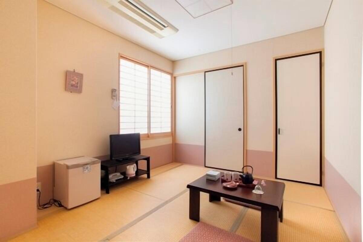 A room with tatami flooring, a television on a stand, a small cabinet, a table with items, and sliding doors.