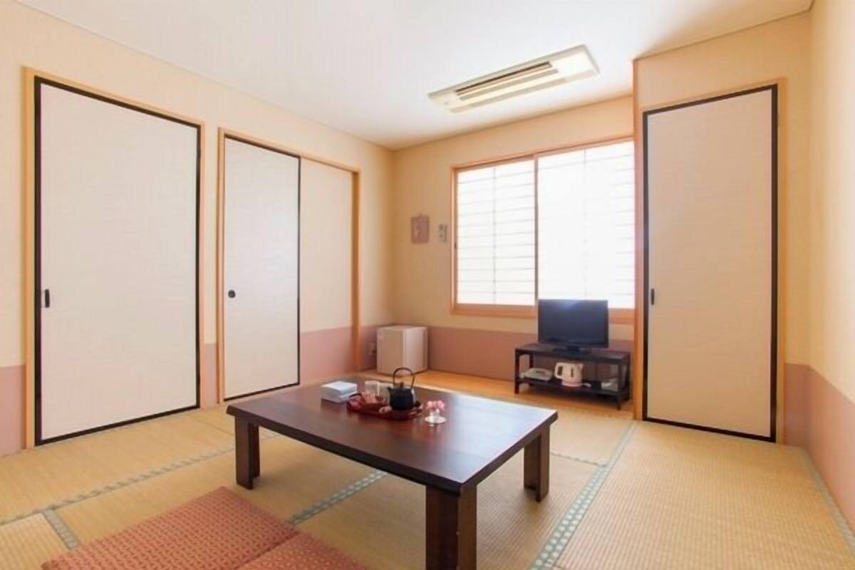 A traditional Japanese room with tatami flooring, sliding doors, a television, and a small table with items on it.