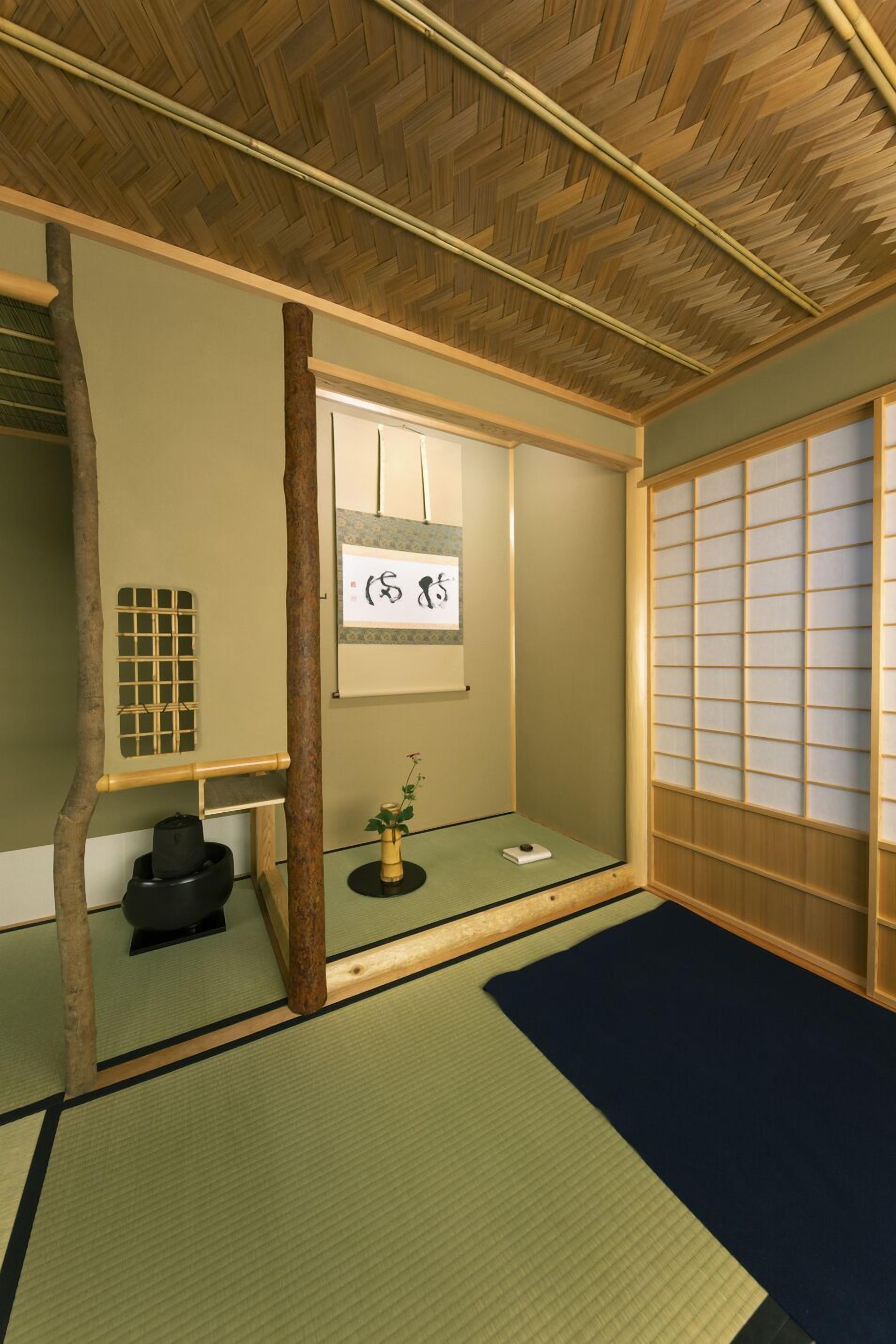 Una habitación japonesa tradicional con suelo de tatami, una pantalla shoji y un pergamino colgante.