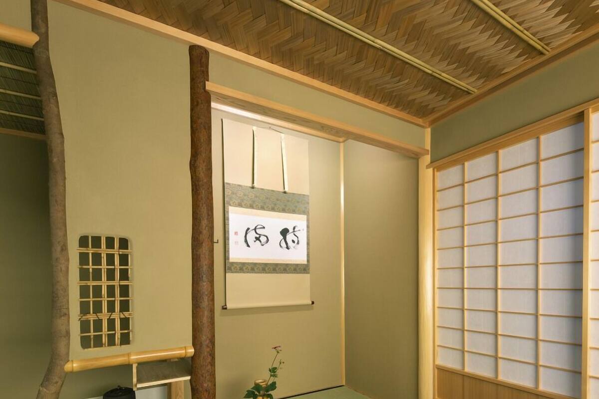 Una habitación japonesa tradicional con suelo de tatami, una pantalla shoji y un pergamino colgante.