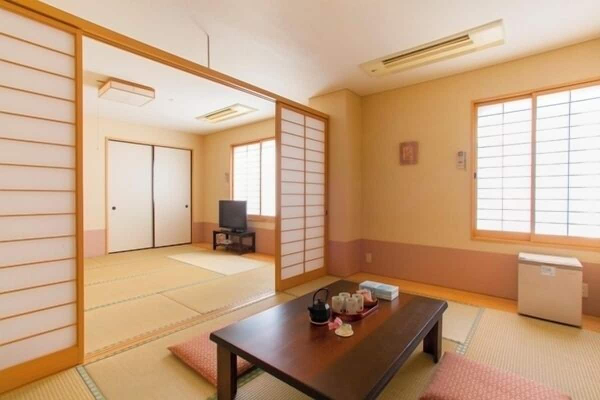 A traditional Japanese room with tatami flooring, a low table with tea set, sliding doors, and a television.