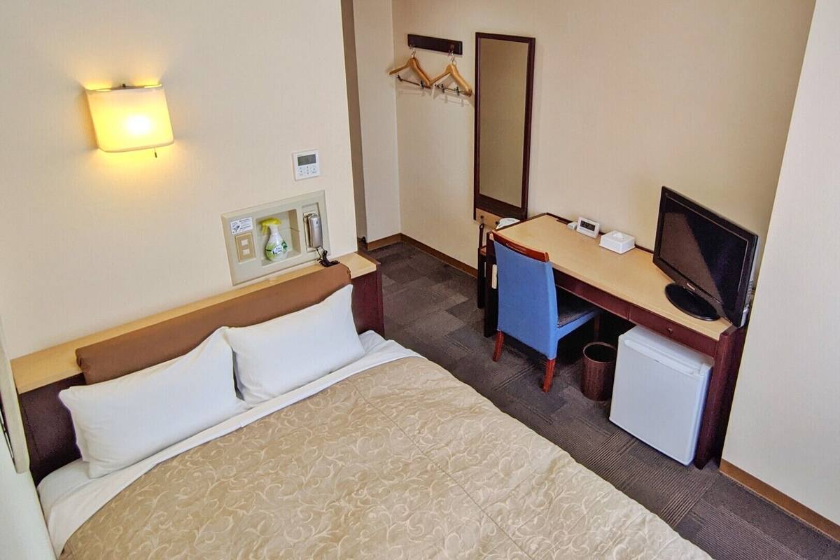 A hotel room with a bed, desk, chair, television, and a small refrigerator.