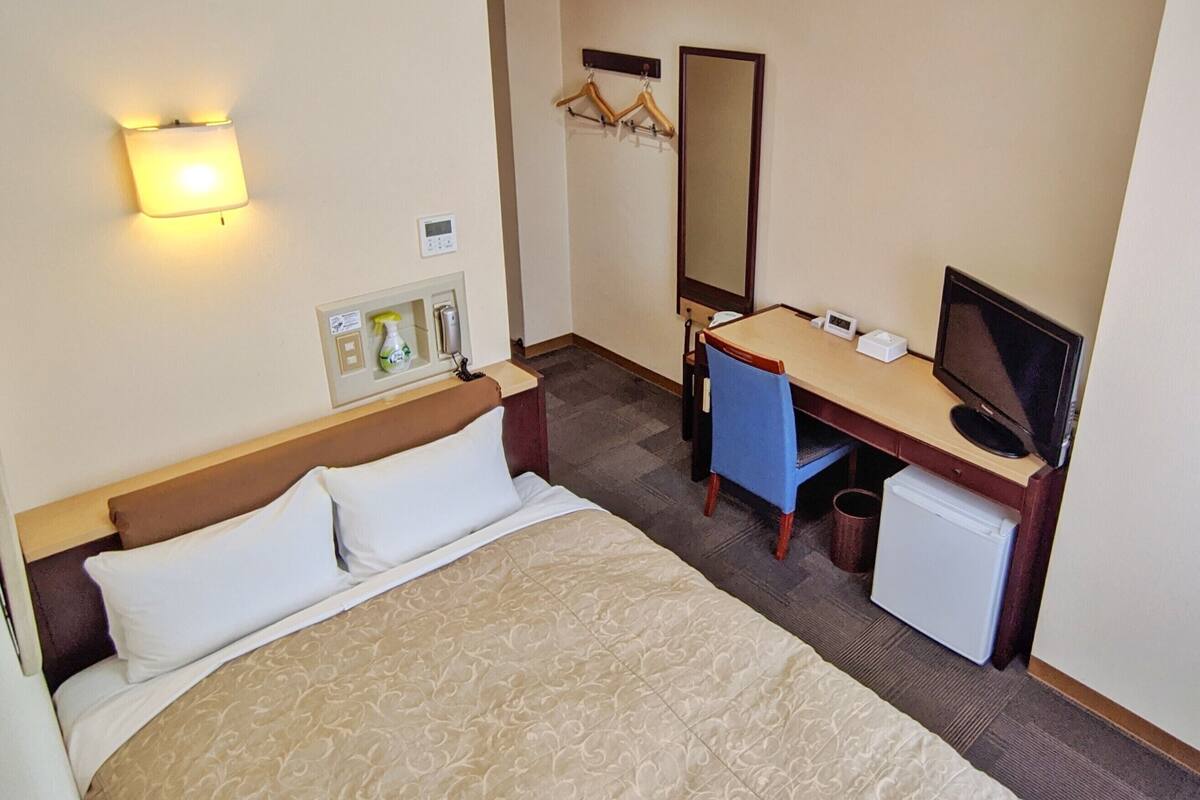 A hotel room with a bed, desk, chair, television, and a small refrigerator.