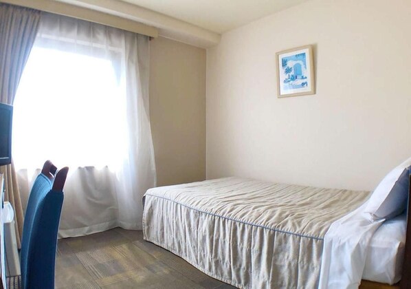 A hotel room with a bed, a chair, a desk, and a window with curtains. - Kadoma Public (Kadoma)