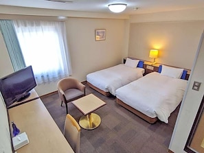 Una habitación de hotel con dos camas, un escritorio con televisión, una silla y una mesita.