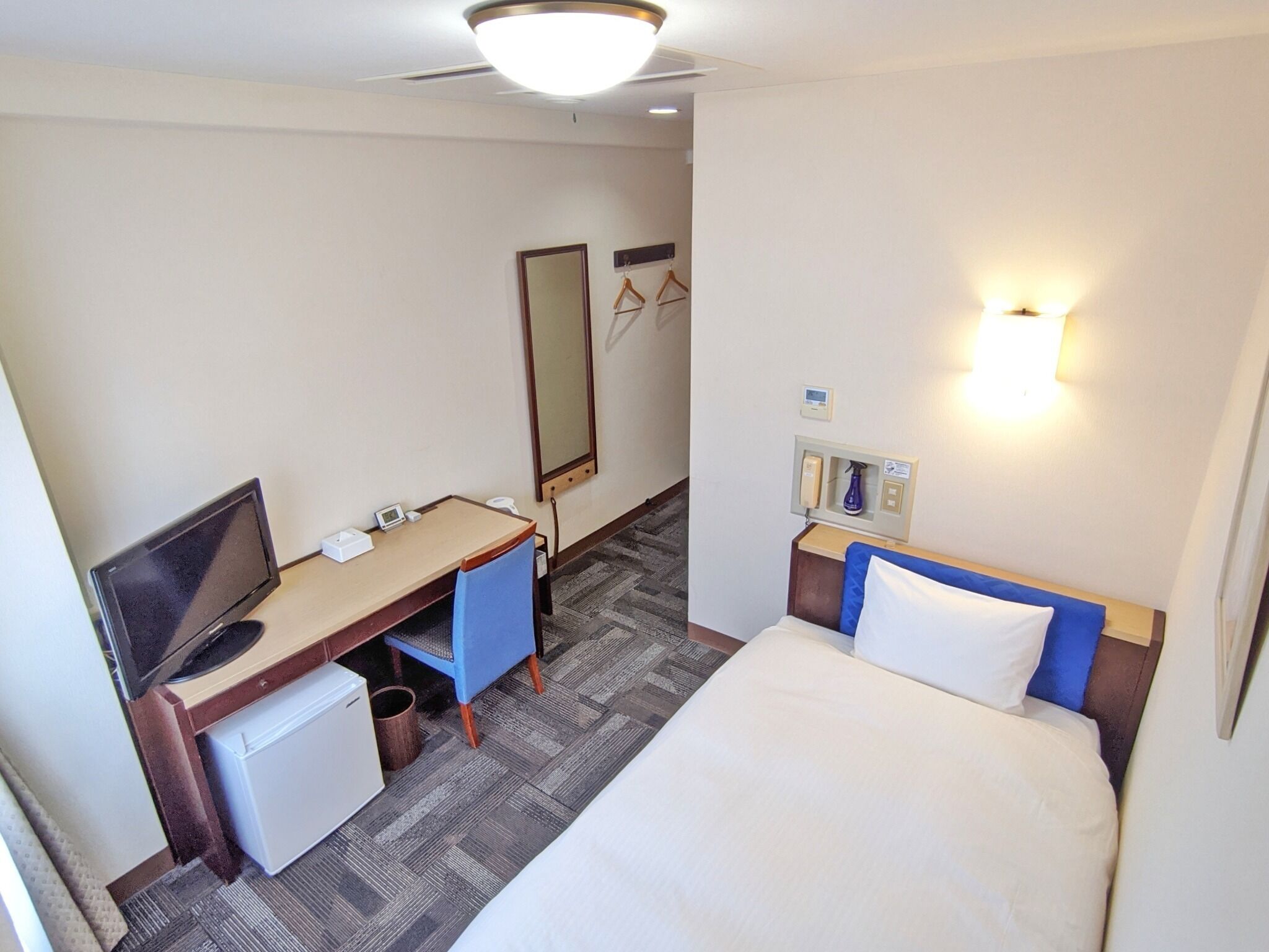 Quarto de hotel com cama, escrivaninha, cadeira, televisão e espelho.