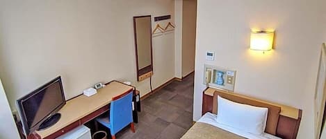 A hotel room with a bed, a desk with a computer, a small fridge, a mirror, and a wall-mounted phone.