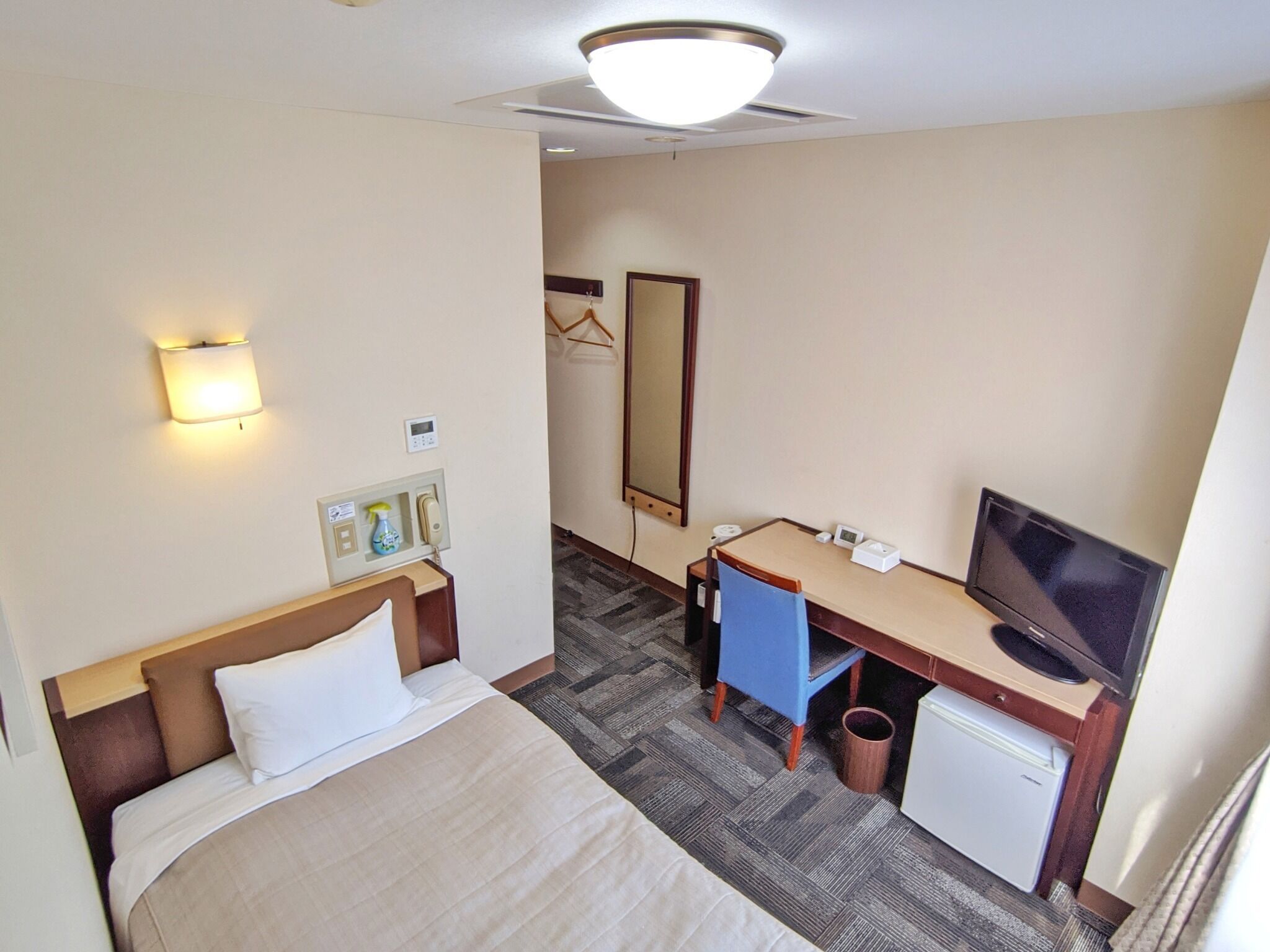 Quarto de hotel com cama, escrivaninha, cadeira, televisão e espelho.