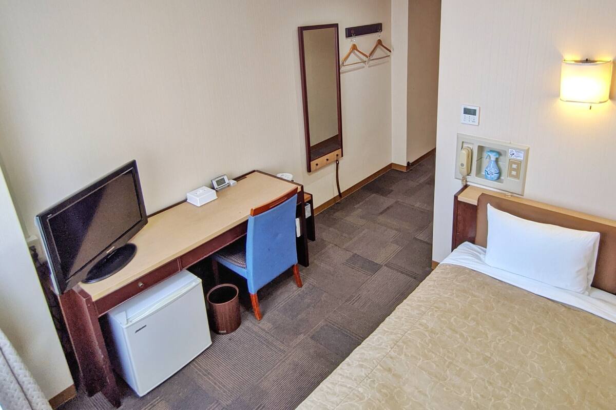 A hotel room with a bed, desk, computer, and a mirror.