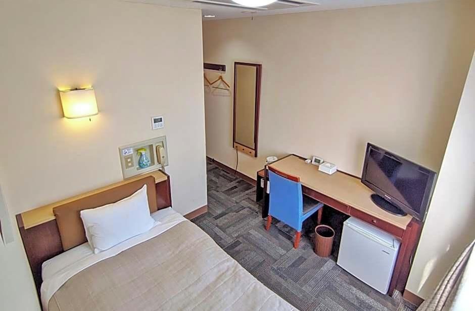 A hotel room with a bed, desk, television, and a small refrigerator.