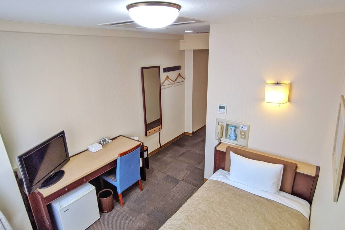 A hotel room with a bed, desk, chair, television, and a small refrigerator.
