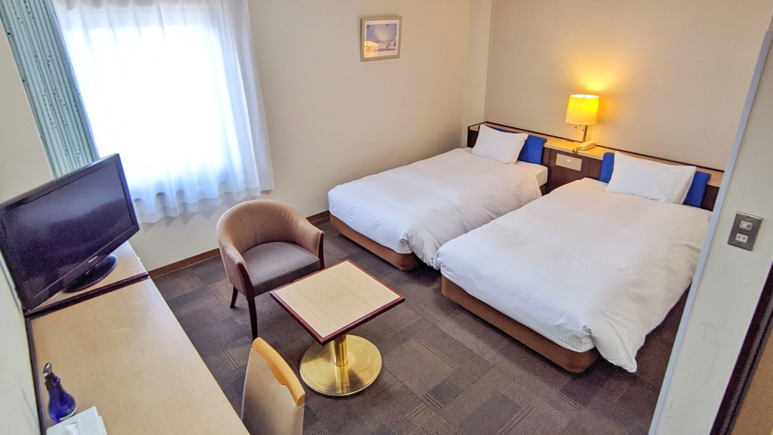A hotel room with two beds, a desk with a chair, a television, and a lamp.