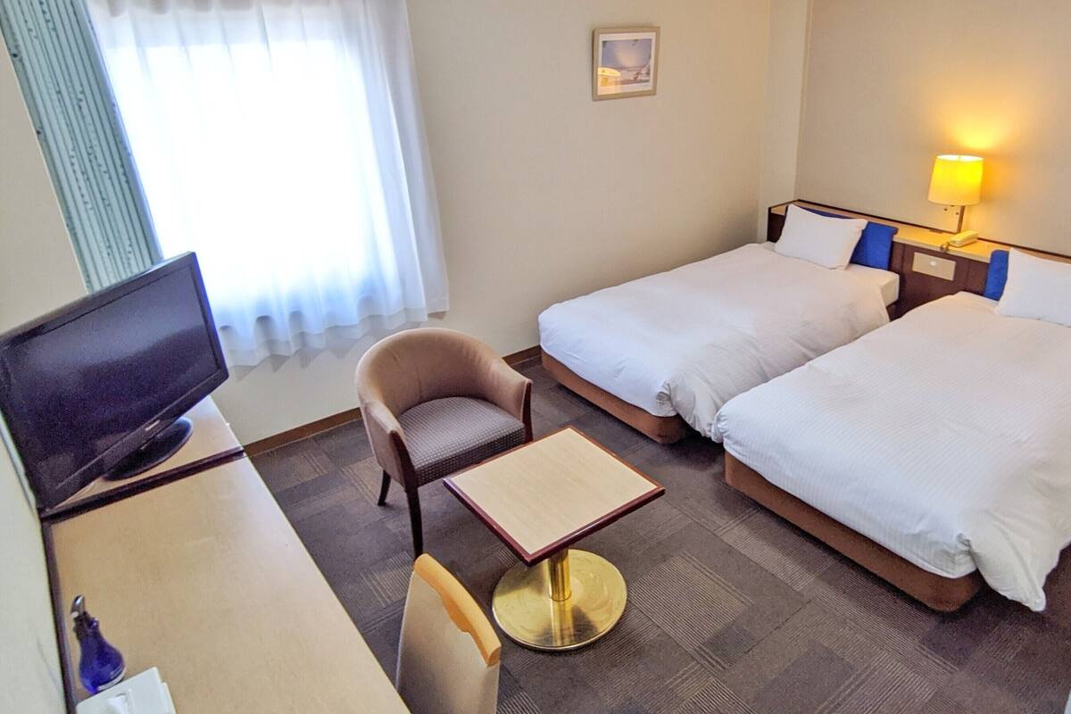 A hotel room with two beds, a desk with a chair, a television, and a lamp.