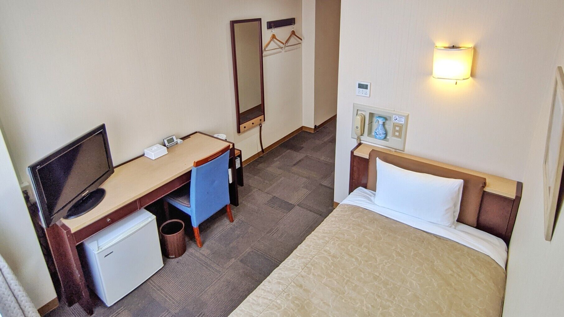 Quarto de hotel com cama, escrivaninha, televisão e mini-geladeira.
