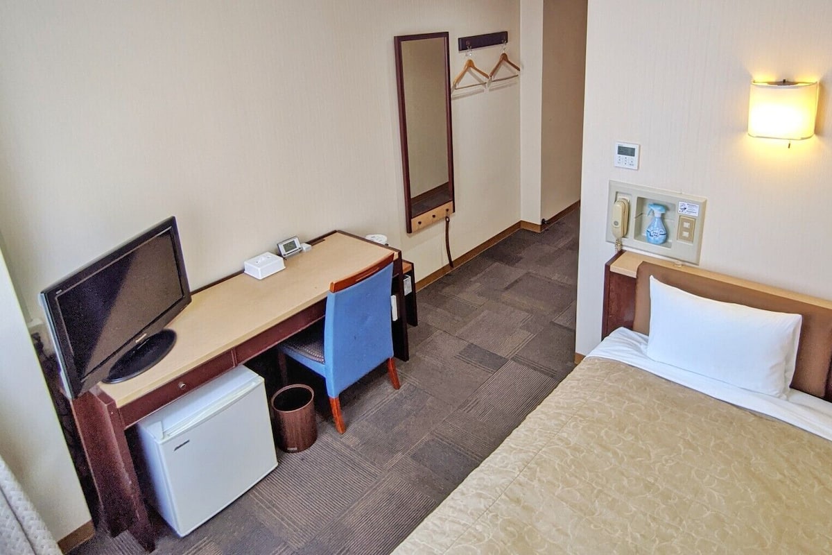 A hotel room with a bed, desk, TV, and a small fridge.