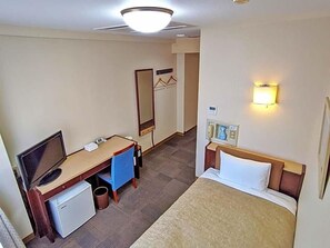 Habitación de hotel con cama, escritorio con computadora, refrigerador pequeño, espejo y lámpara de pared.