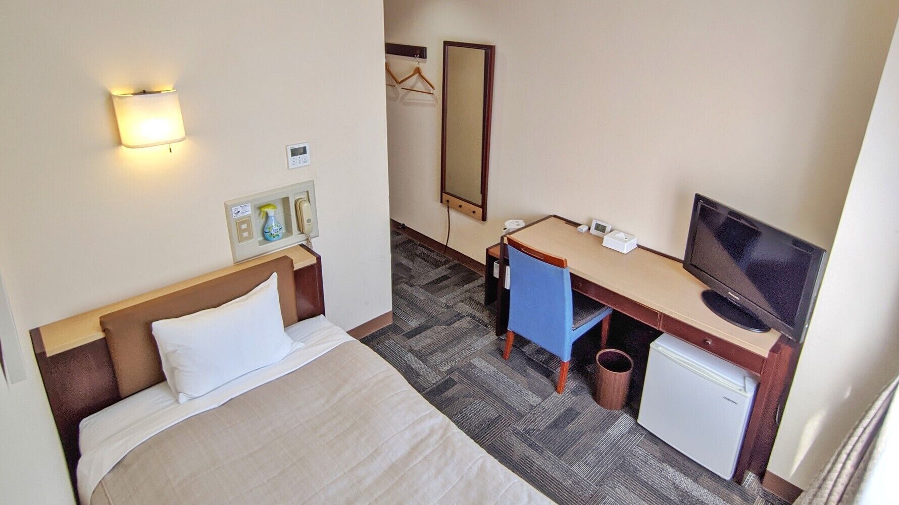 Quarto de hotel com uma cama, uma escrivaninha com computador, televisão e espelho.