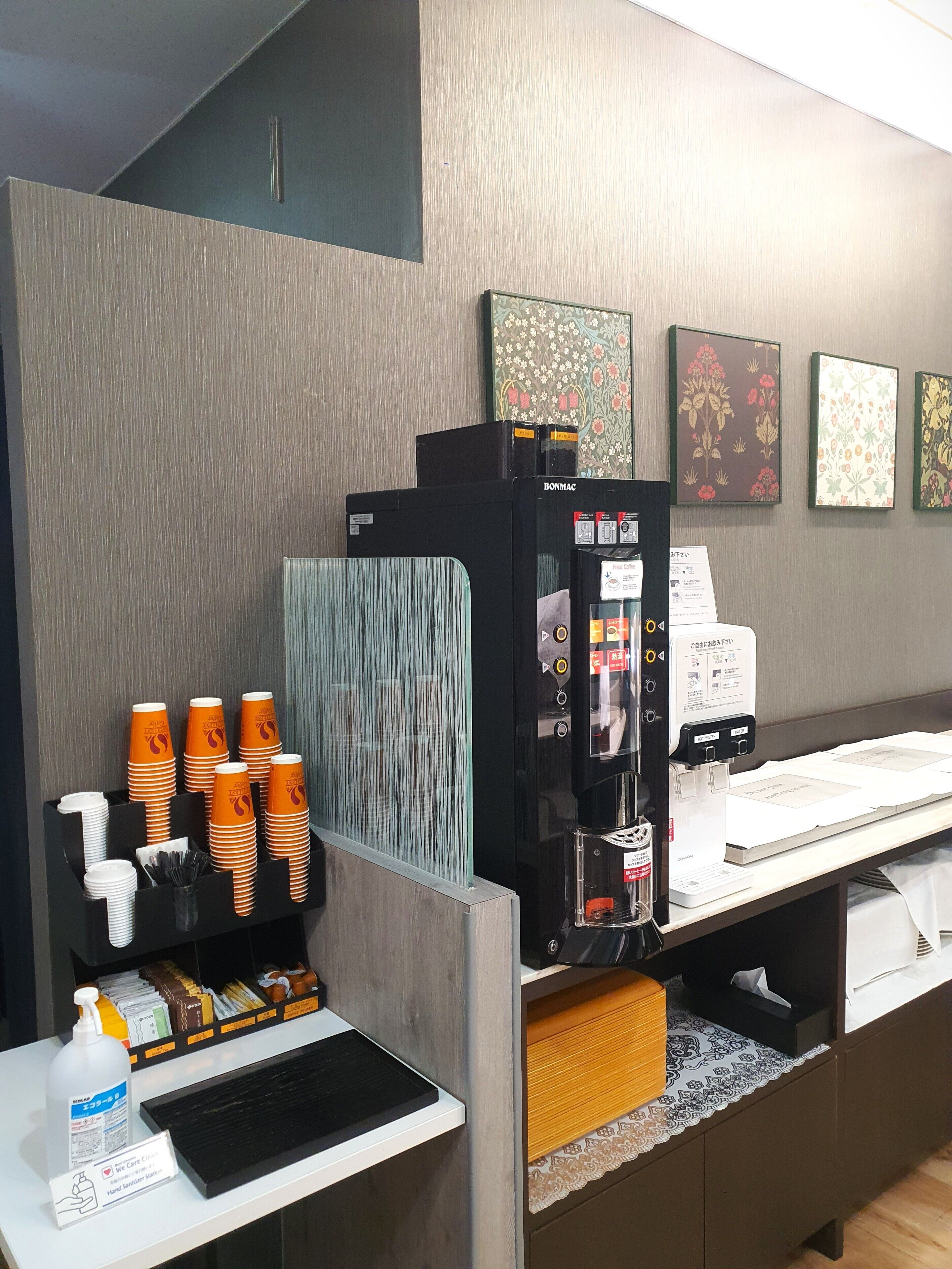 Ein Hotel-Rezeptionsbereich mit einer Kaffeemaschine, Handdesinfektionsmittel und einem Menüausgabegerät.