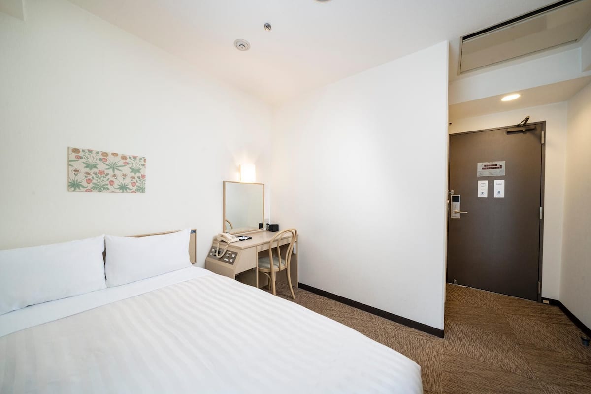 Ein Hotelzimmer mit Bett, Schreibtisch, Stuhl und einer Tür mit einem Schild.
