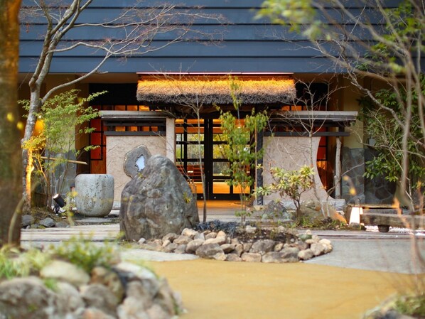 A traditional building with a thatched roof entrance, large rocks, and a stone pathway leading to the door.