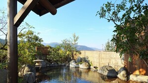 Un jardín tranquilo con un estanque, rodeado de rocas y plantas, y una valla de madera al fondo.
