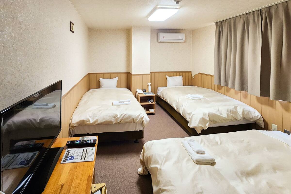 Habitación de hotel con dos camas, un escritorio con computadora, un televisor y un equipo de aire acondicionado.