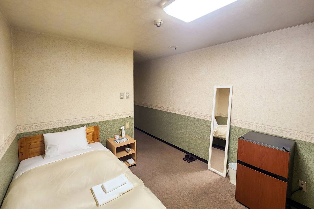 Una habitación de hotel con una cama, una mesita de noche, un espejo, un aparador y una puerta que da a otra habitación.