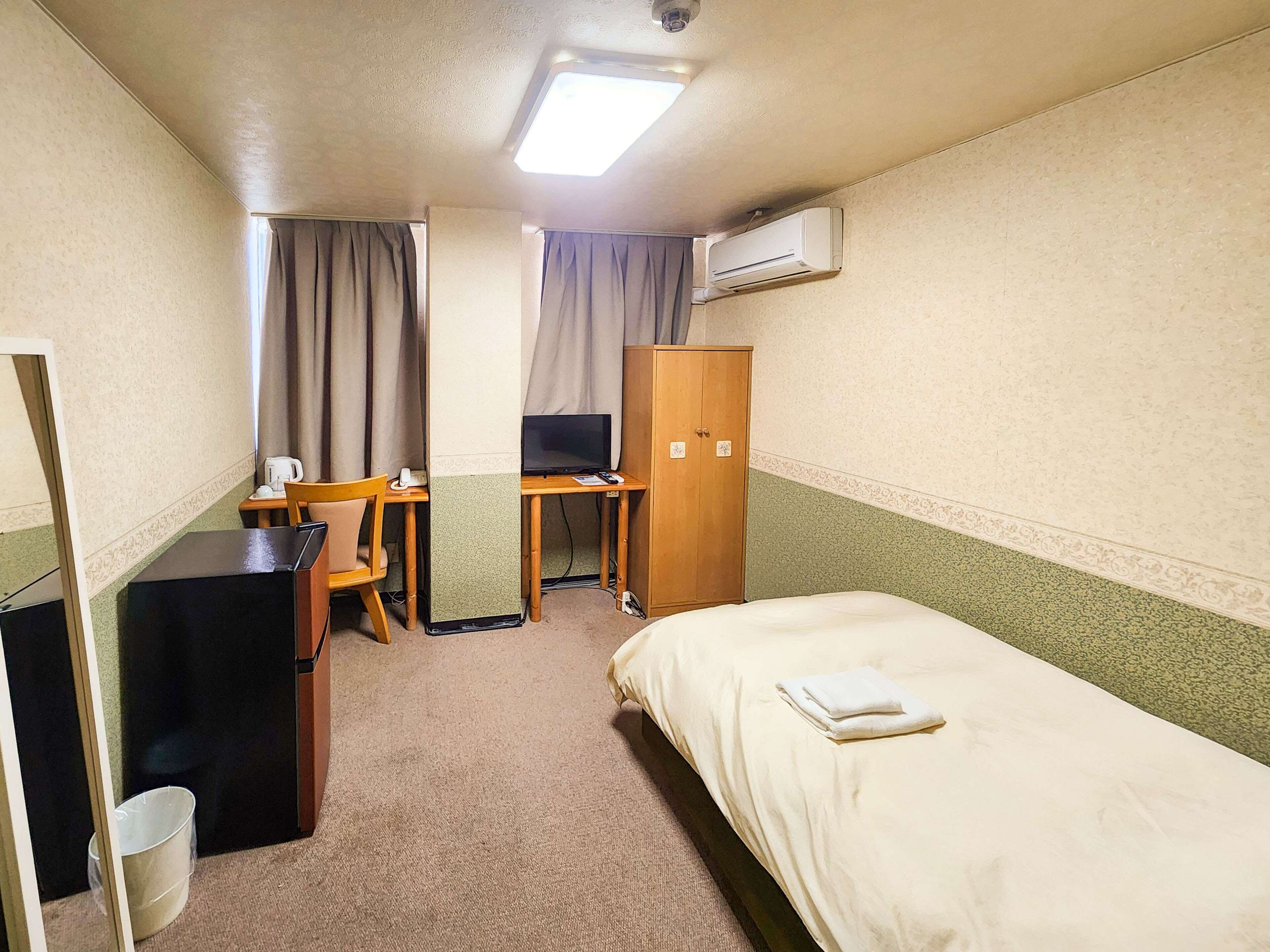 Ein Hotelzimmer mit einem Bett, einem Schreibtisch mit Computer, einem Kleiderschrank und einem kleinen Tisch mit Wasserkocher.