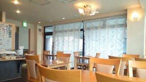 Un espace repas avec des tables et des chaises en bois, un comptoir avec un ordinateur et des documents, et une fenêtre ornée de rideaux blancs.