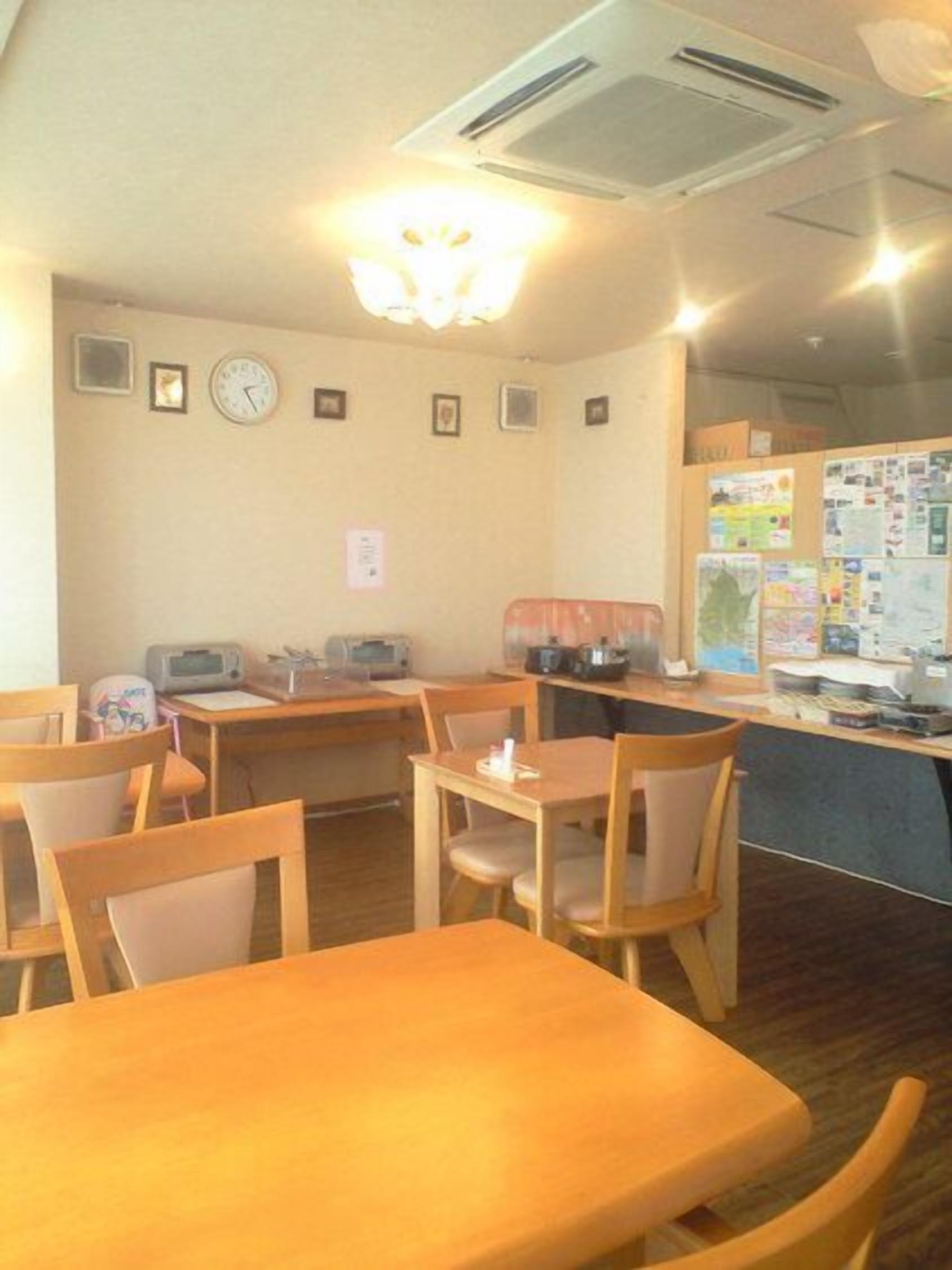 A dining area with wooden tables and chairs, a wall-mounted clock, and a bulletin board with various papers.