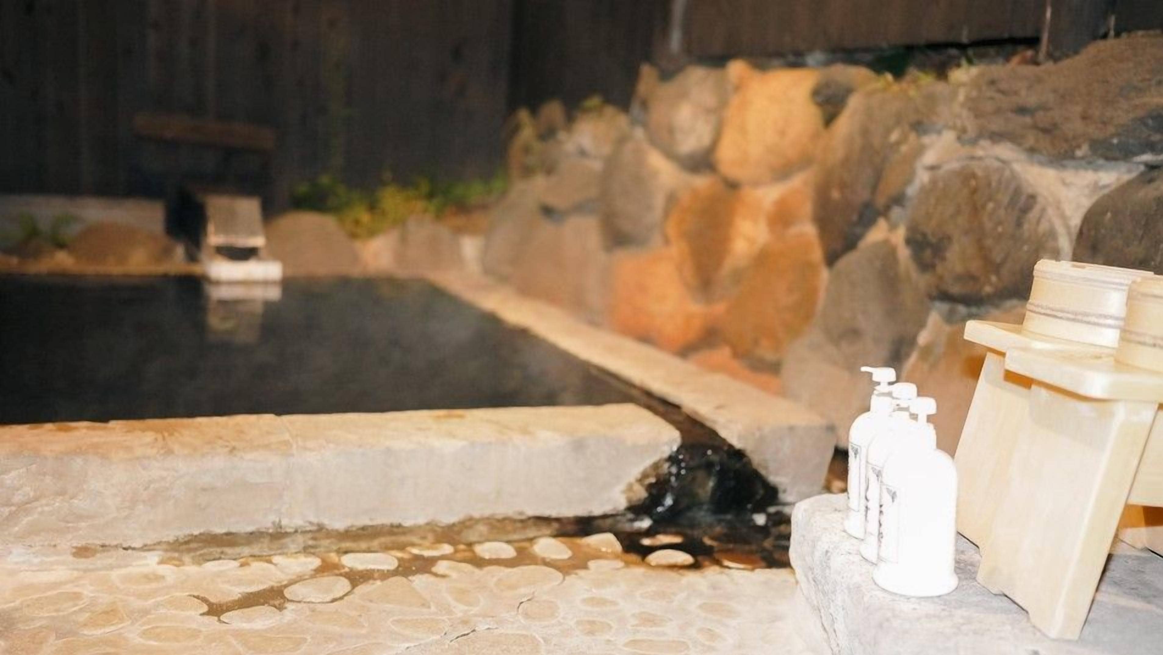 A stone pool with a waterfall feature, surrounded by rocks and a wooden structure.