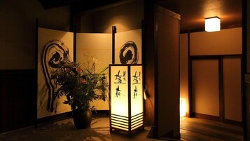 Una habitación japonesa tradicional con suelo de tatami, un shoji con caligrafía y un farol encendido.