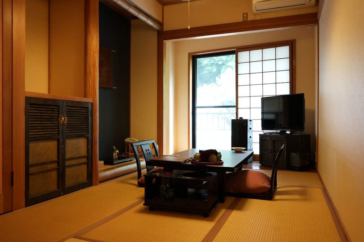 A traditional Japanese room with tatami flooring, a low table with cushions, a television, and sliding doors.