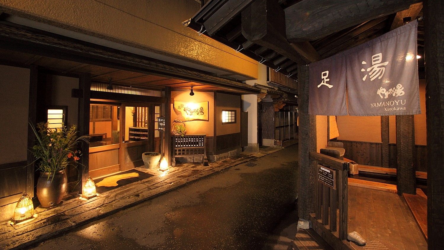 A traditional Japanese establishment with a wooden exterior, a signboard, and a lantern-lit pathway.