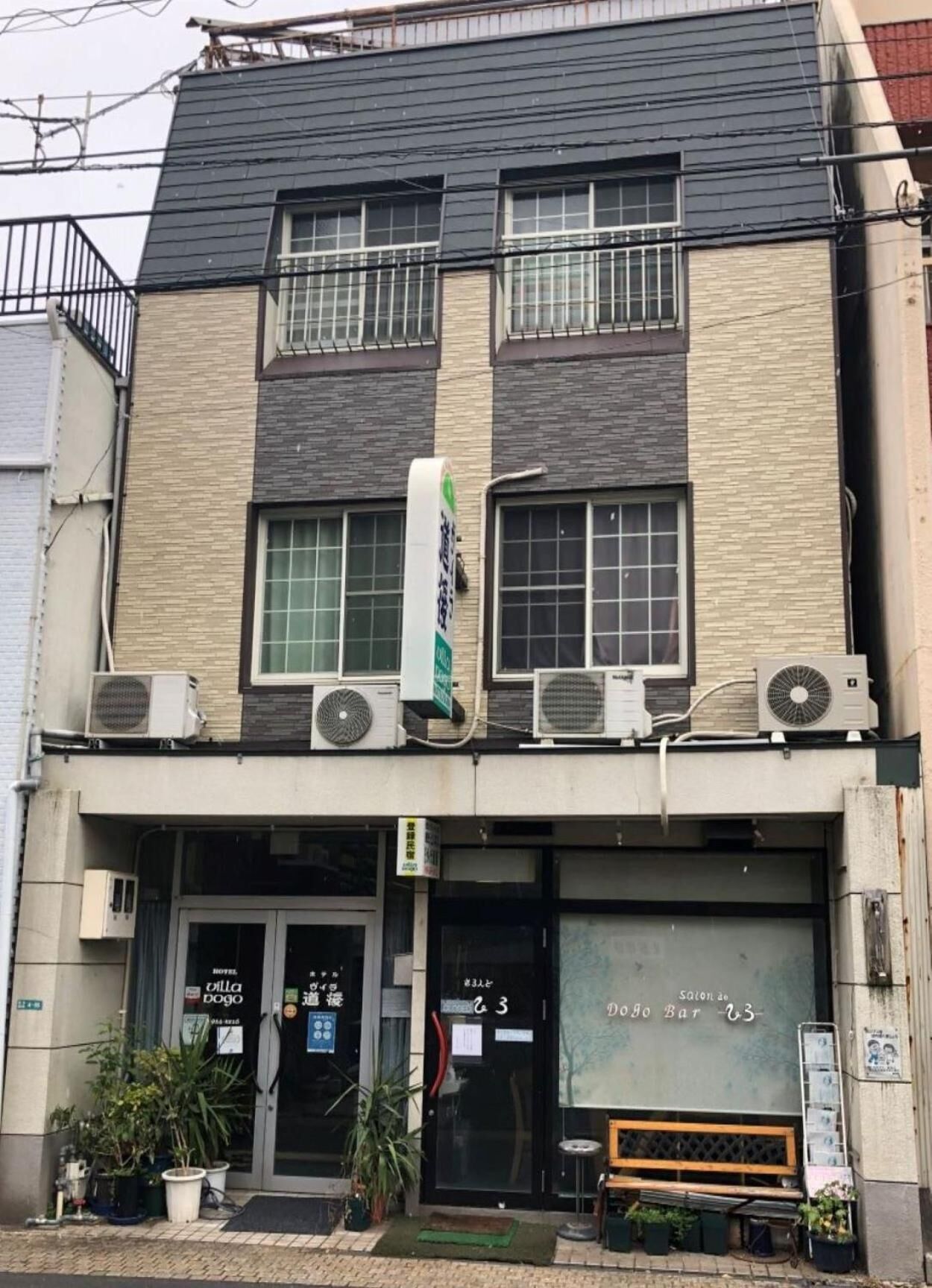 A two-story building with air conditioning units on the roof, a signboard, and a bench outside.