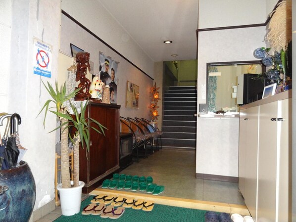 A hotel lobby with a staircase, a reception desk, and a row of green slippers on the floor. - Villa Dogo (Matsuyama)